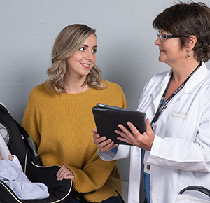 Woman with baby in carrier talking to healthcare provider.